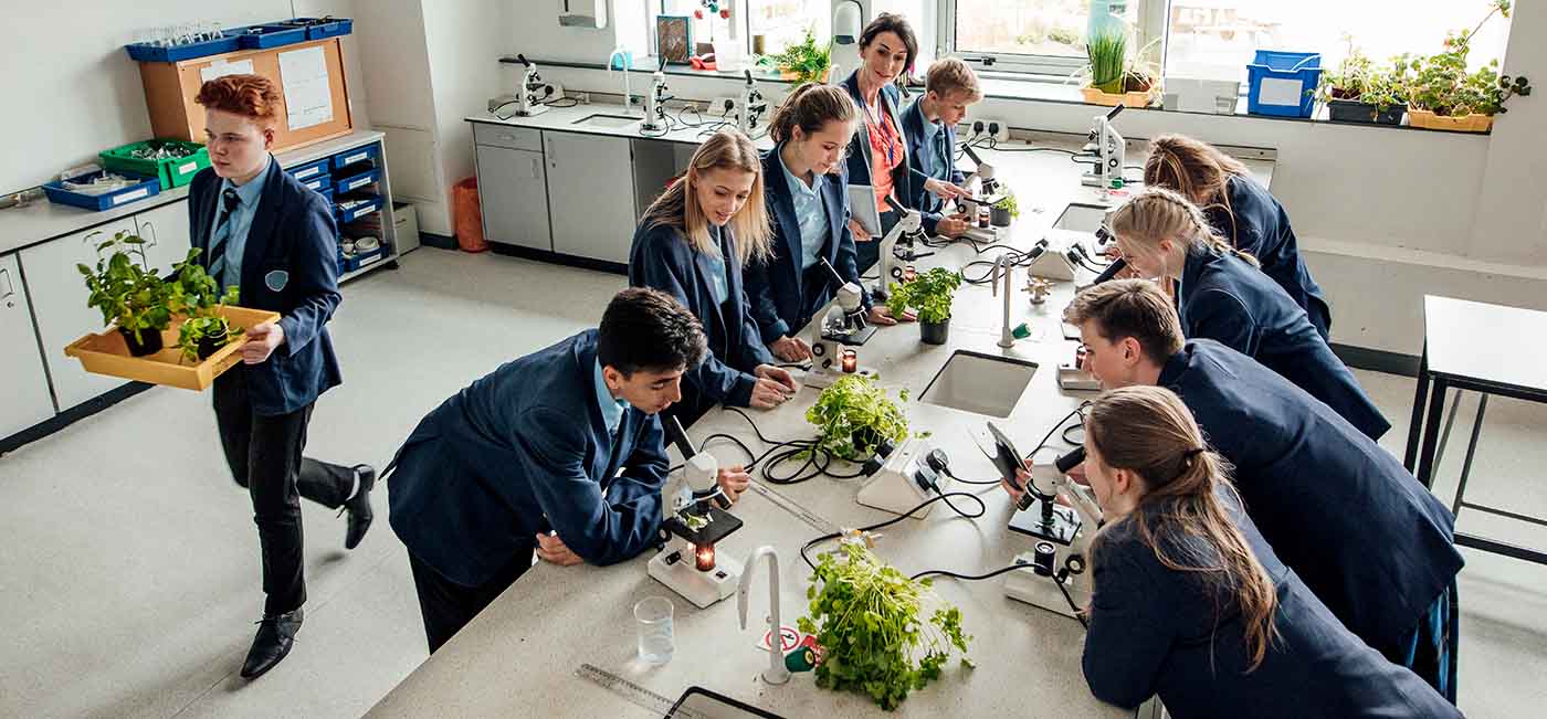 High school students in science class with teacher examining plants with microscopes