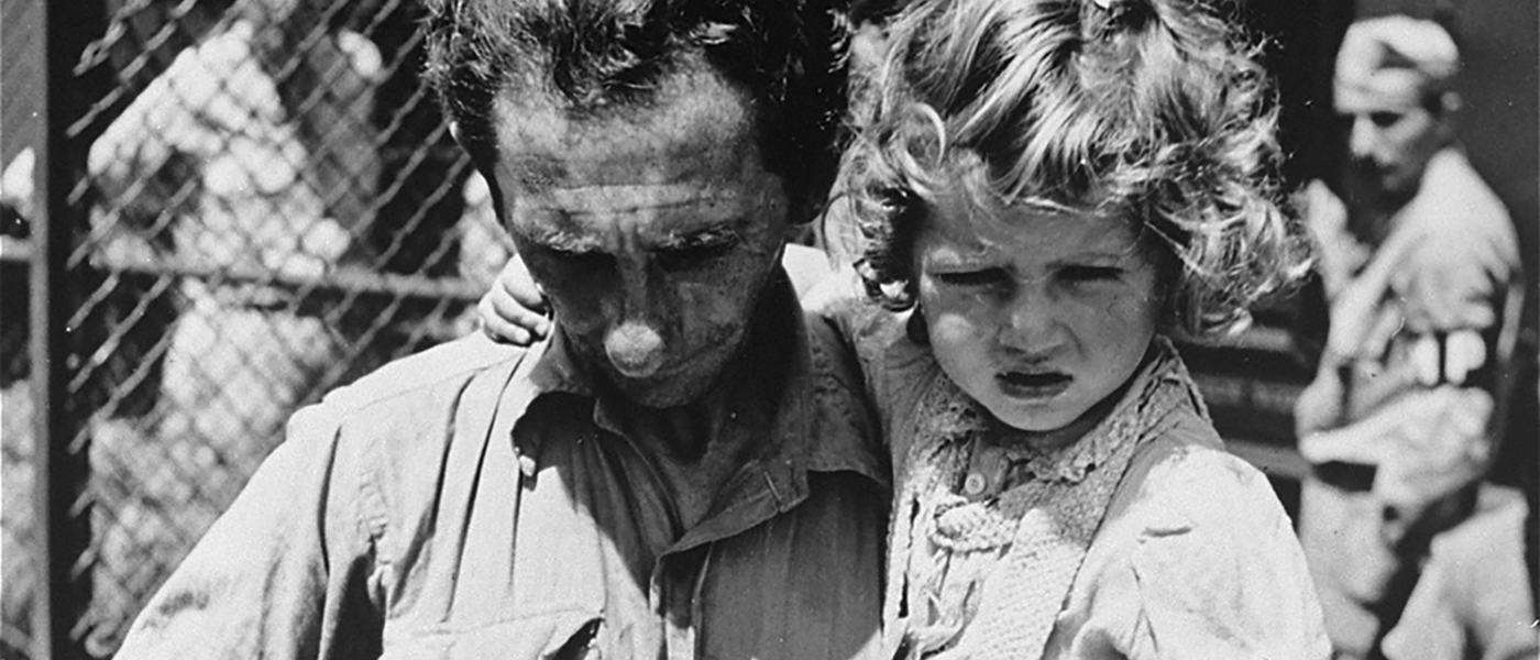 A father, holding his daughter, checks his tags during check in at the Fort Ontario refugee shelter.!''